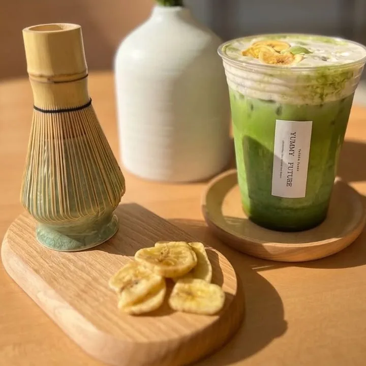 Matcha Banana Einspanner beside a bamboo whisk and banana chips