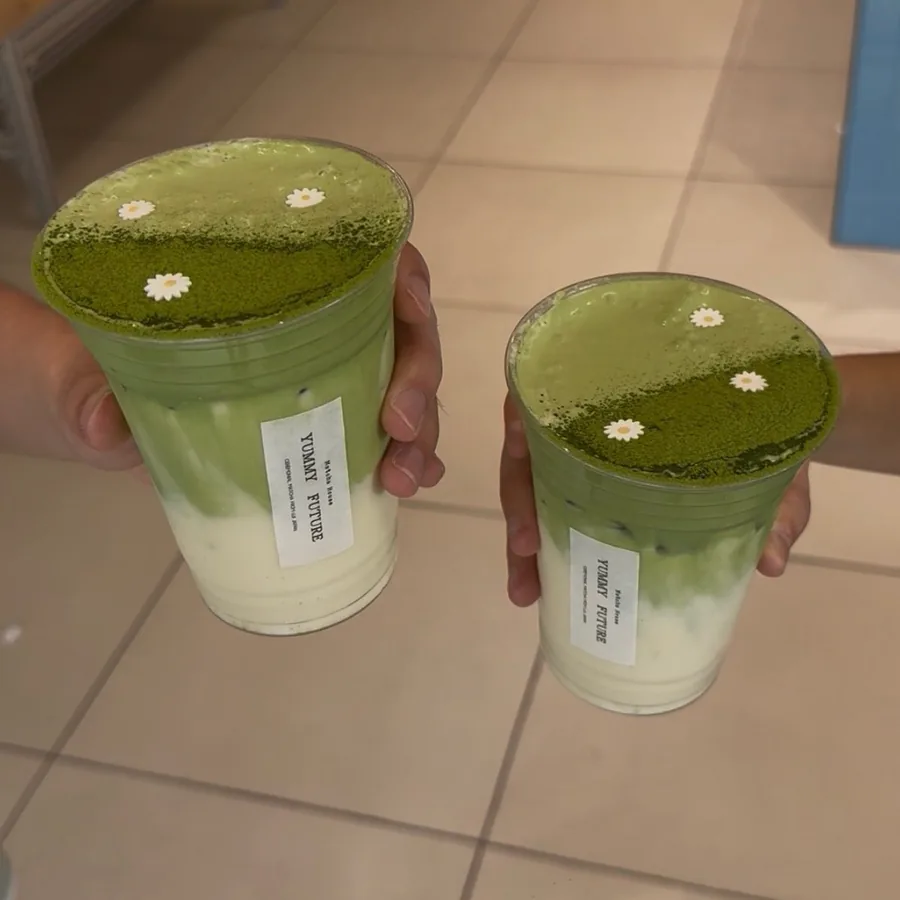 Two matcha lattes held up inside the shop, tables in the background