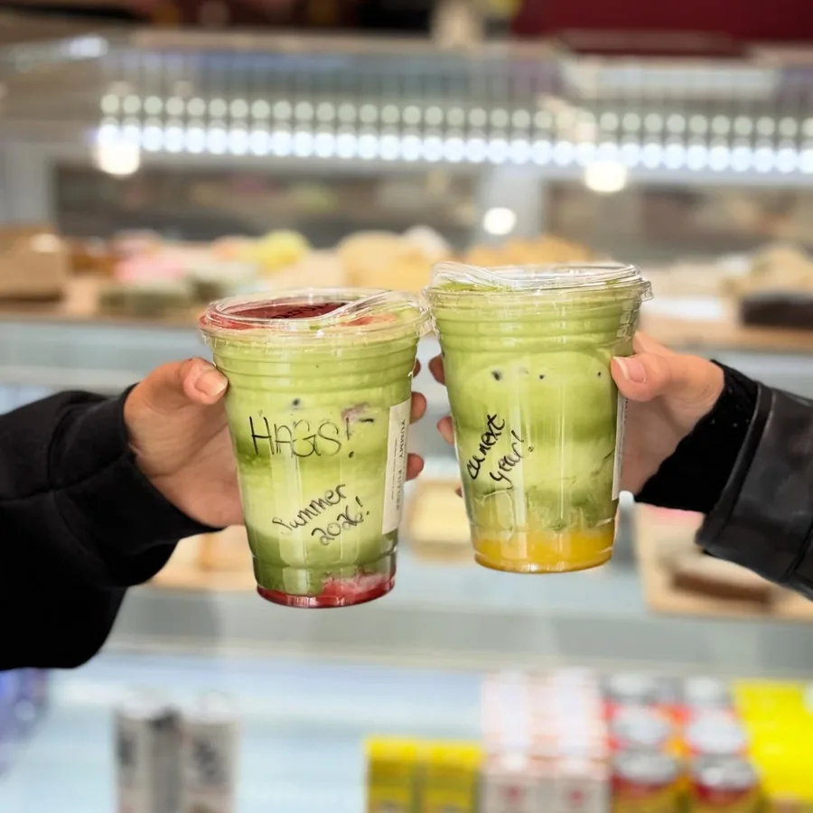 Two matcha drinks held up in front of the pastry case at the counter