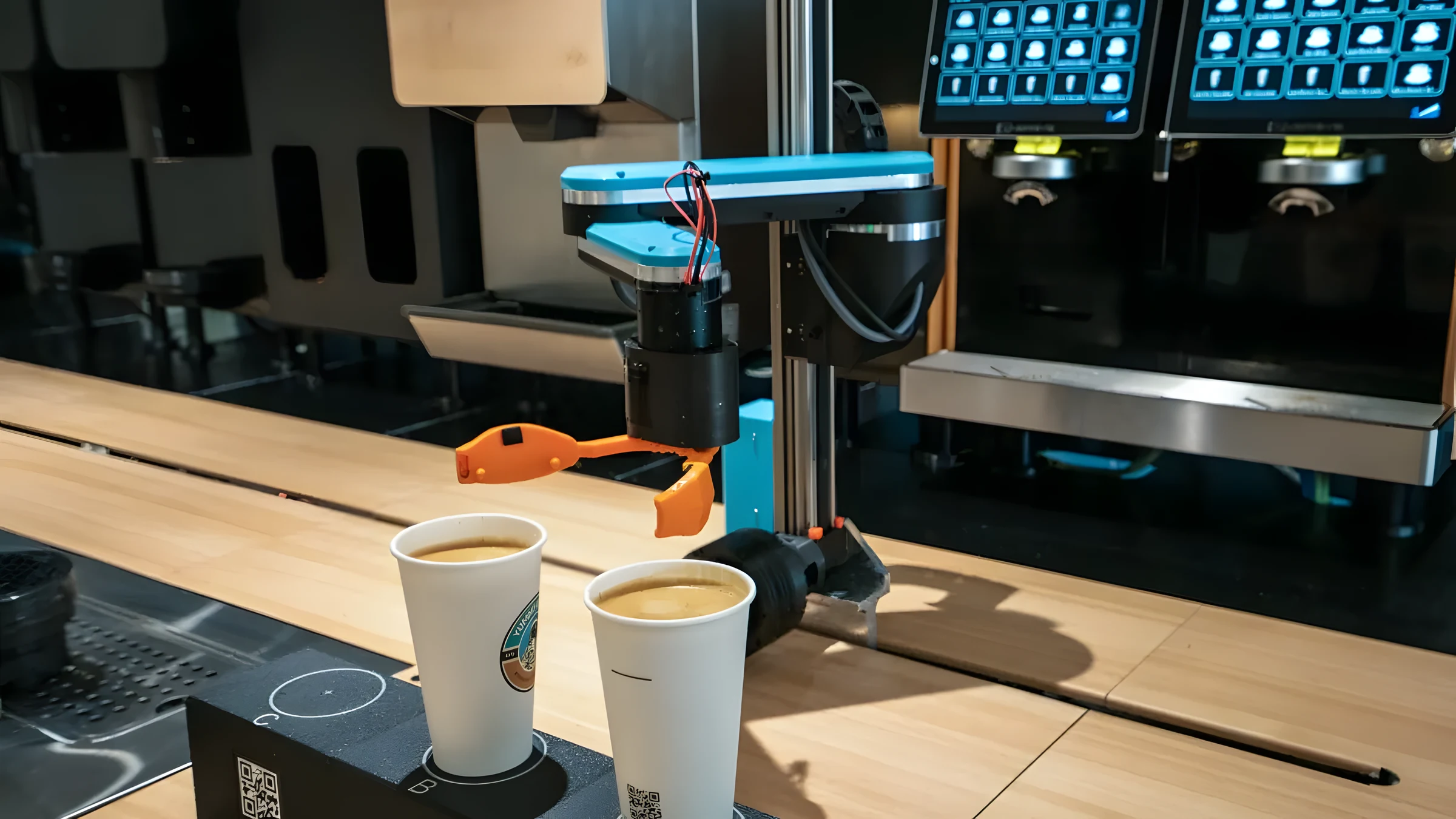 Robotic arm positioning two cups under the espresso heads