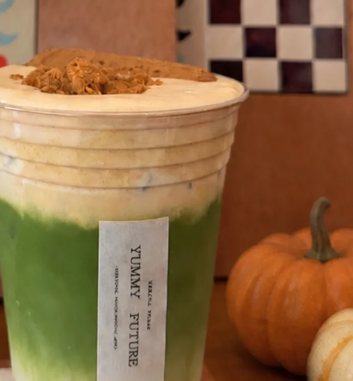 A layered pumpkin matcha latte next to small pumpkins